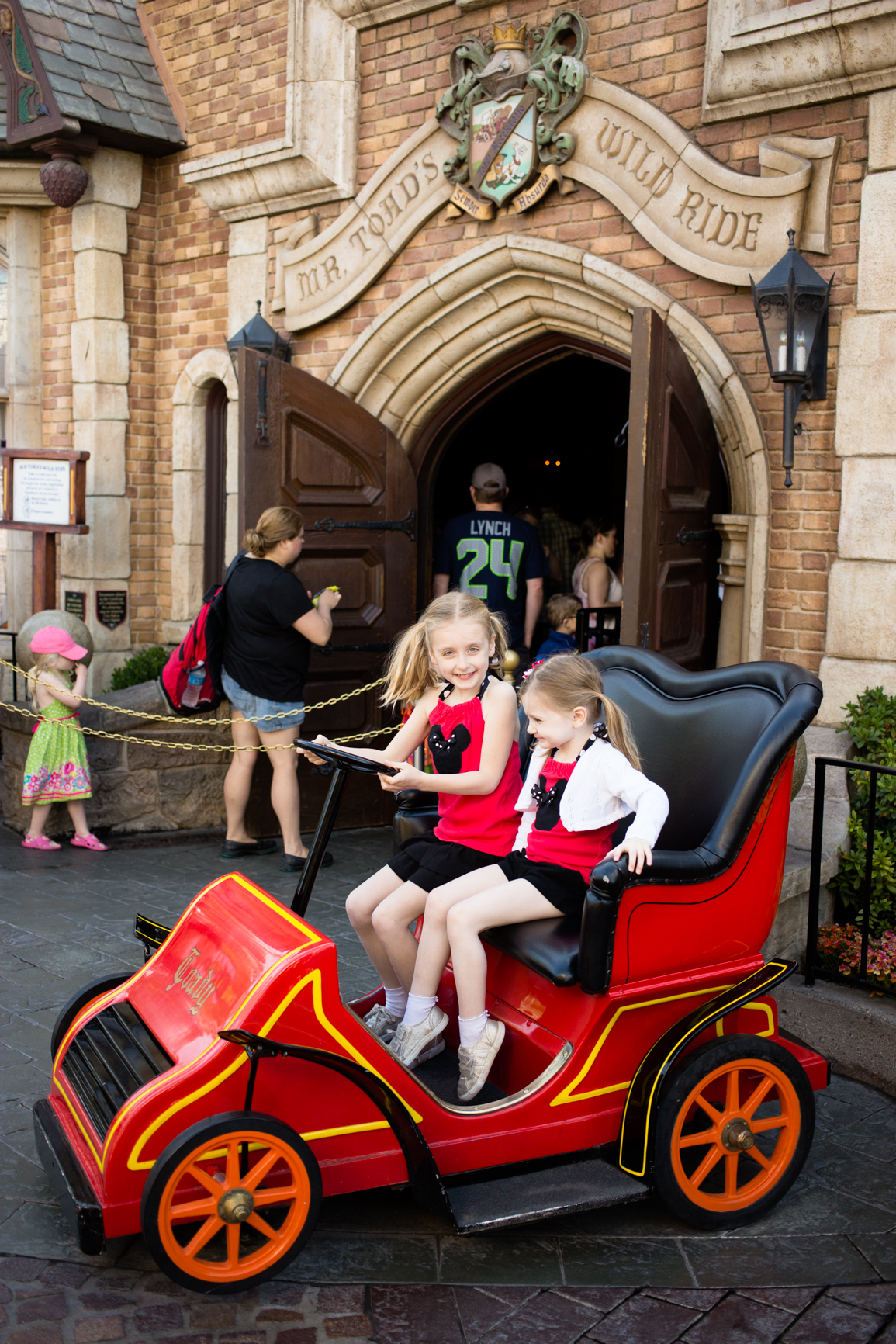 Two girls sit in a sample red car outside the ride.
