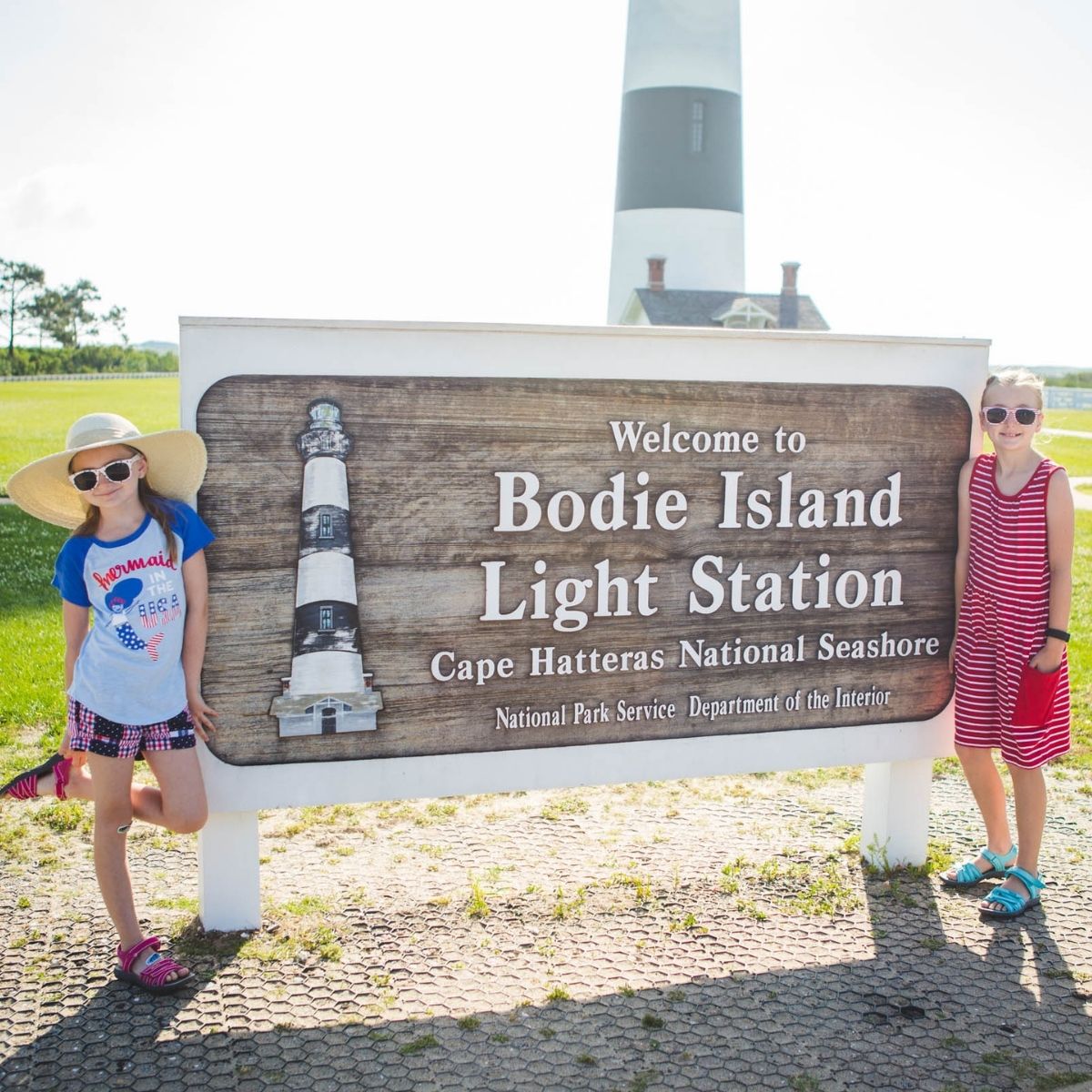 Two young girls stand by the welcome sign at the Bodie Island Light House.