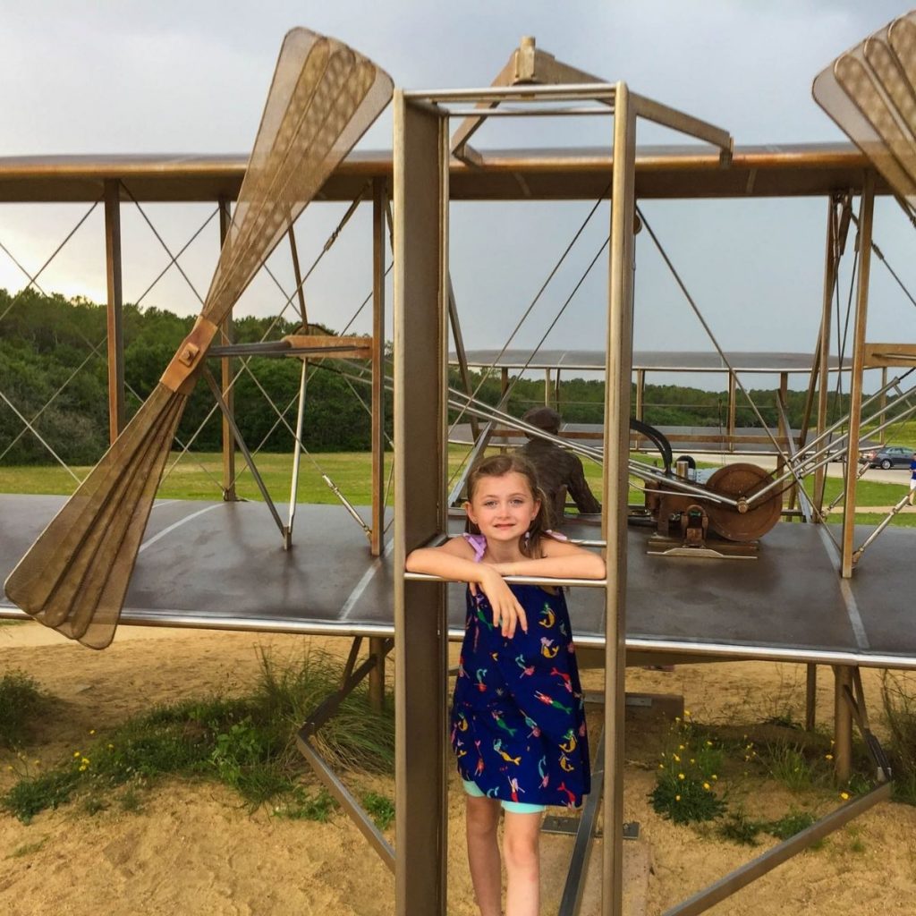 A young girl stands by a model plane at the Wright Brothers Memorial