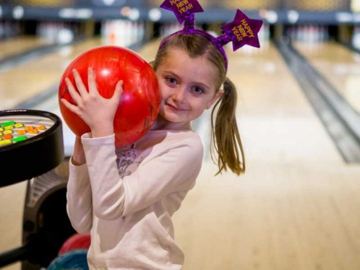 A young girl holds a large bowling ball on a bowling lane in Charlotte.