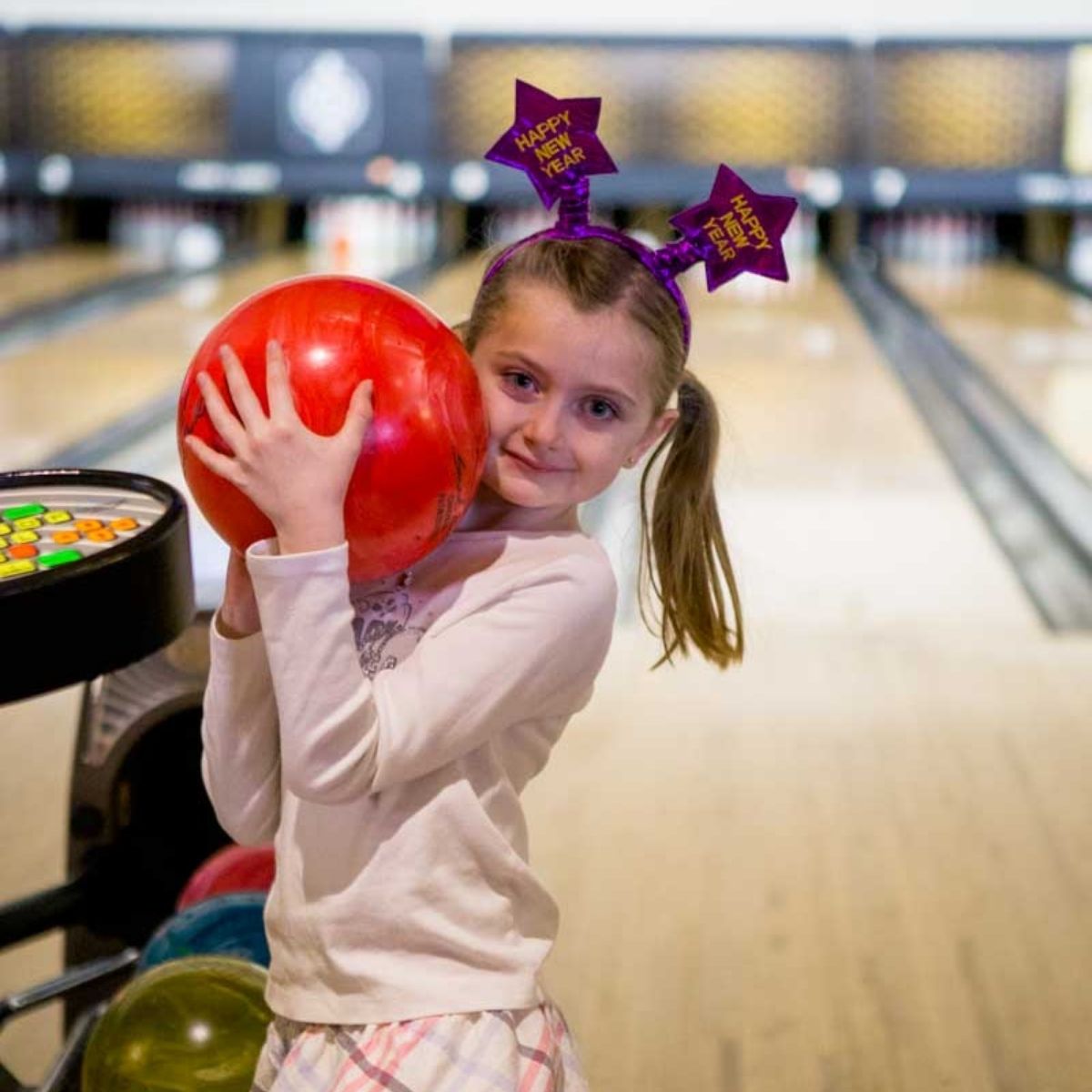 A young girl holds a large bowling ball on a bowling lane in Charlotte.