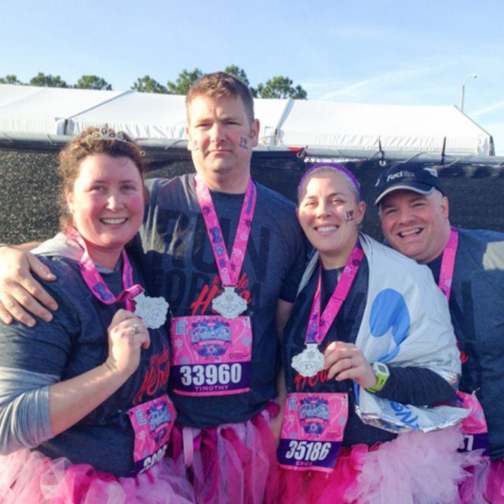 4 friends pose with their Disney metals after a race, everyone is wearing pink tutus.