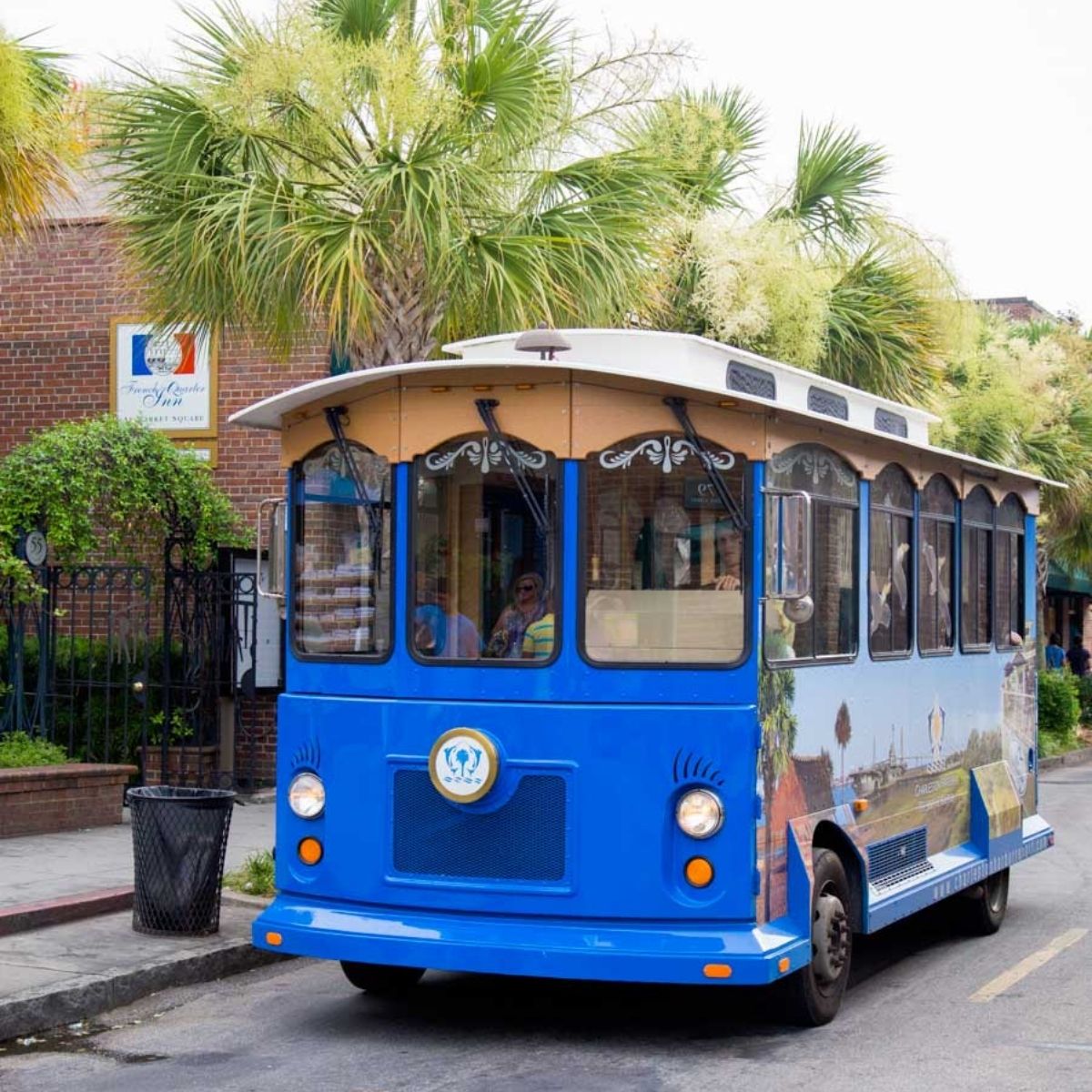 A blue tourist bus driving in Charleston with palm trees in the background.