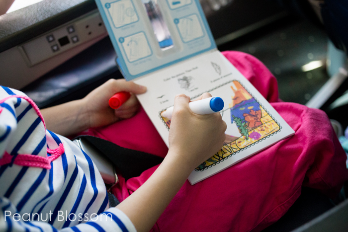 A young girl colors in an activity book on an airplane.