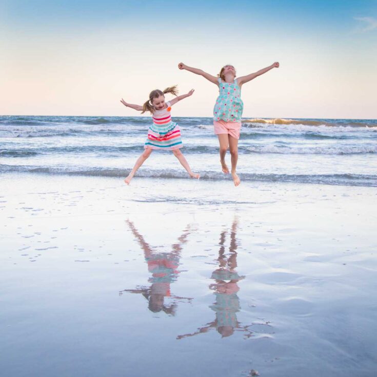 Two young girls are having fun jumping at the beach.
