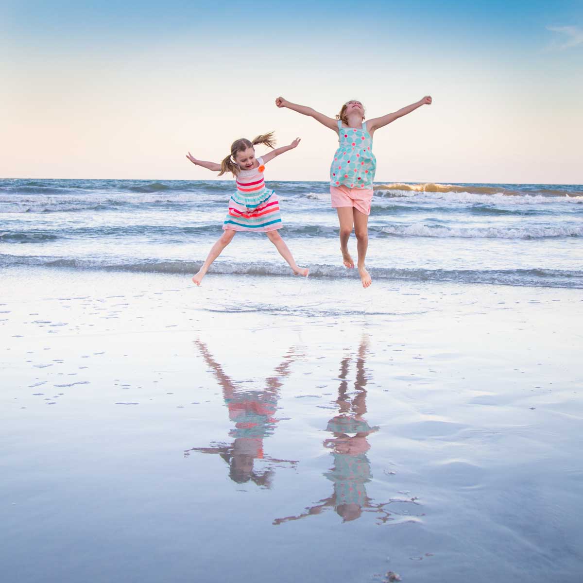 Two young girls are having fun jumping at the beach.