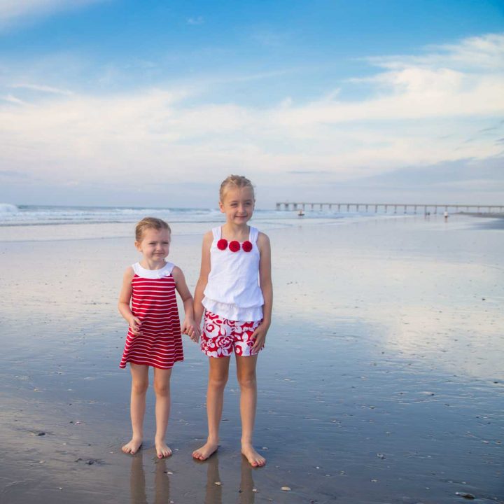A pair of young sisters hold hands on the beach.