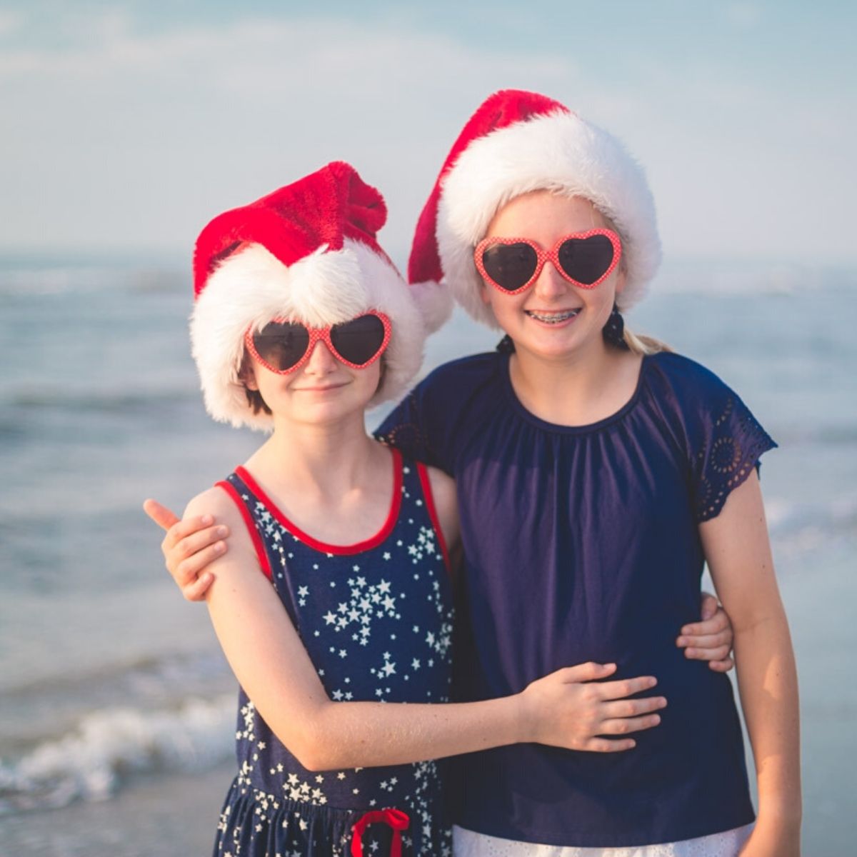 Two girls at the beach wearing Santa hats.
