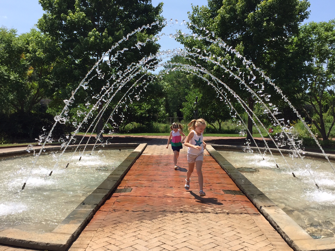 Two young girls run through the fountain arch.
