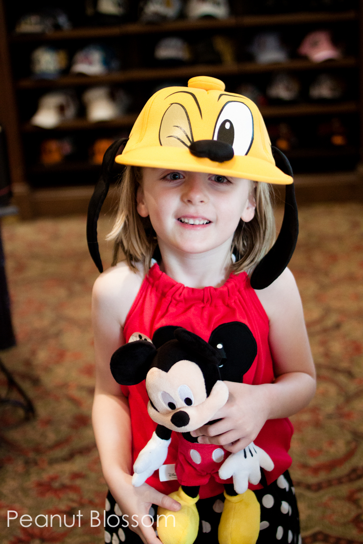 A young girl tries on a Pluto hat while holding a Mickey Mouse toy.