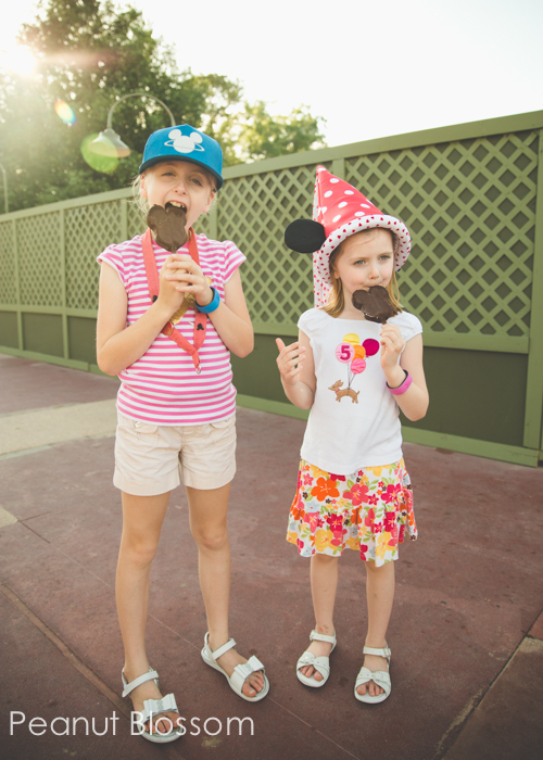 Two girls eating Mickey Mouse shaped pops.