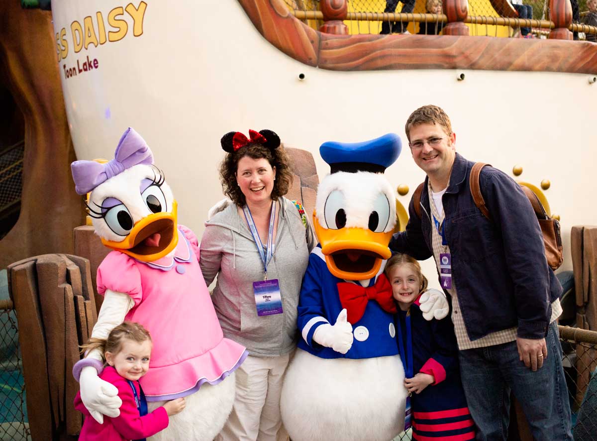 A mom & dad pose with their kids and Donald and Daisy Duck