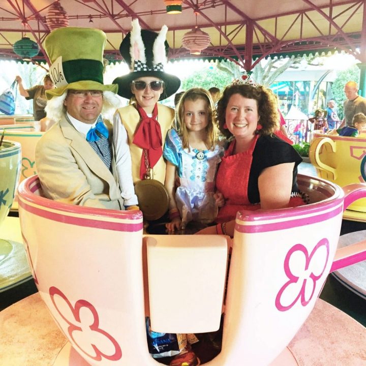 A family dressed in Alice in Wonderland costumes sits in the tea cup ride