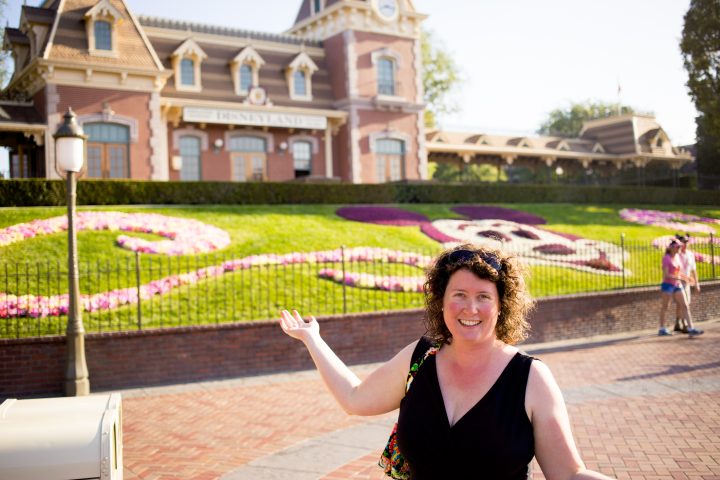 A mom poses outside the entrance to Disneyland.