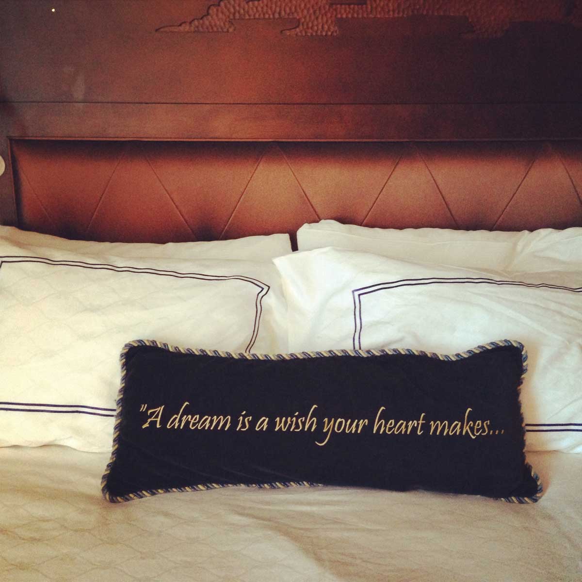 An embroidered pillow on a hotel bed.