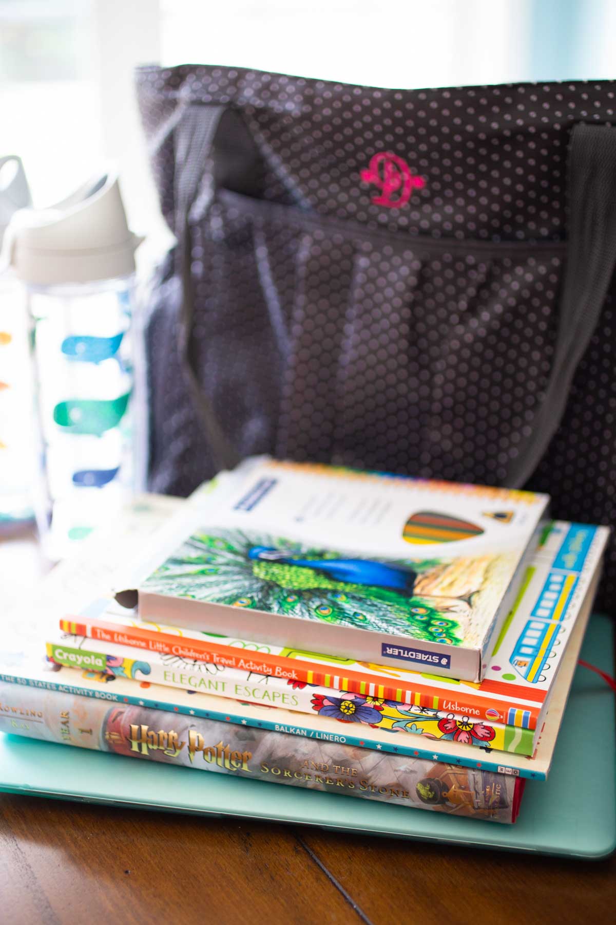 A multipurpose totebag has a pile of books and a water bottle next to it.