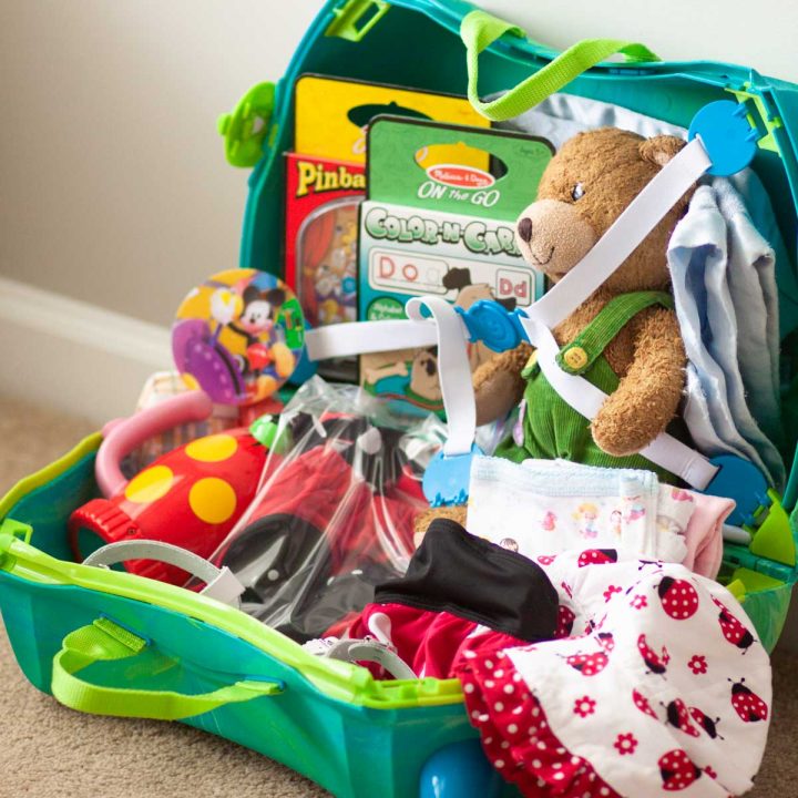 A kids' suitcase is filled with clothing and a few toys.