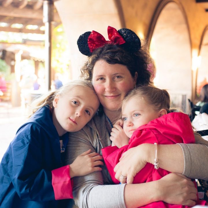 A mom wearing Minnie ears poses for a vacation photo with her two daughters.