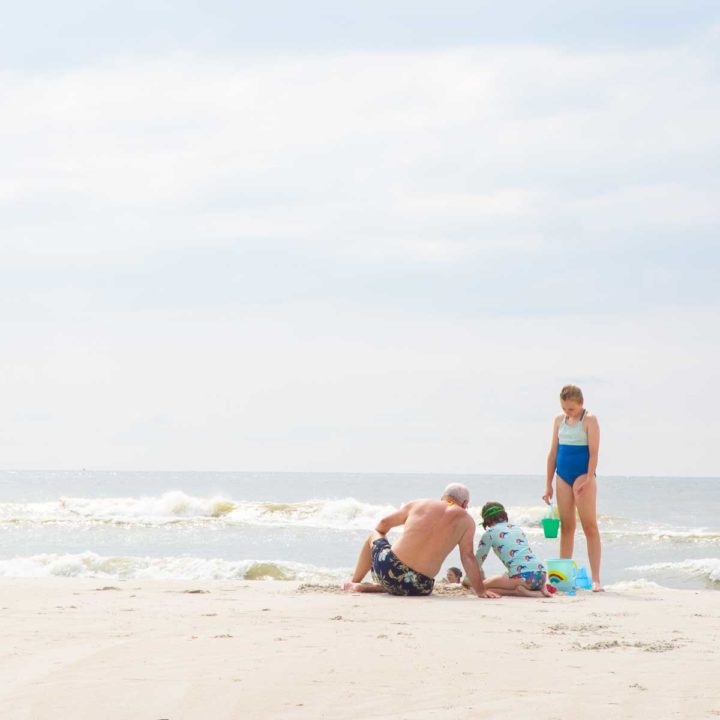 A grandpa and two girls make sandcastles on the beach.