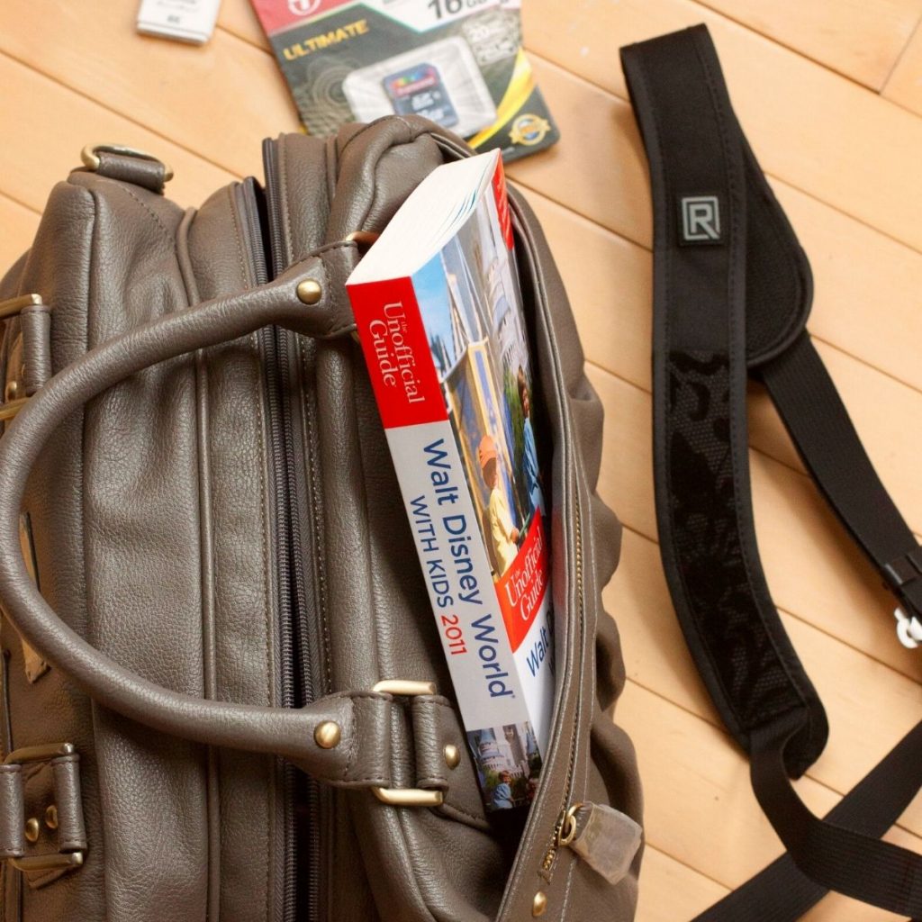A camera bag has a photo book peeking out of the pocket and a camera strap on the ground next to it.