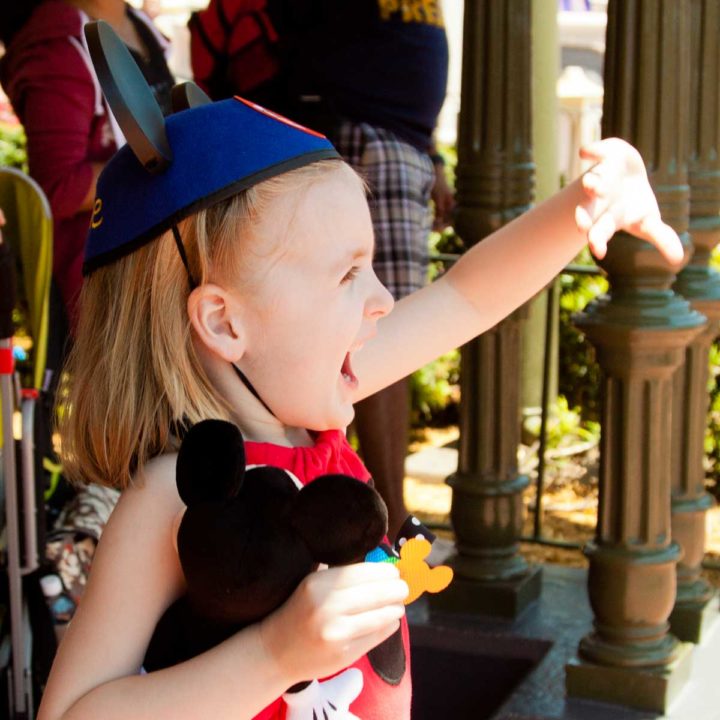 A young girl wearing Mickey ears waves at Mickey Mouse at Disney World.