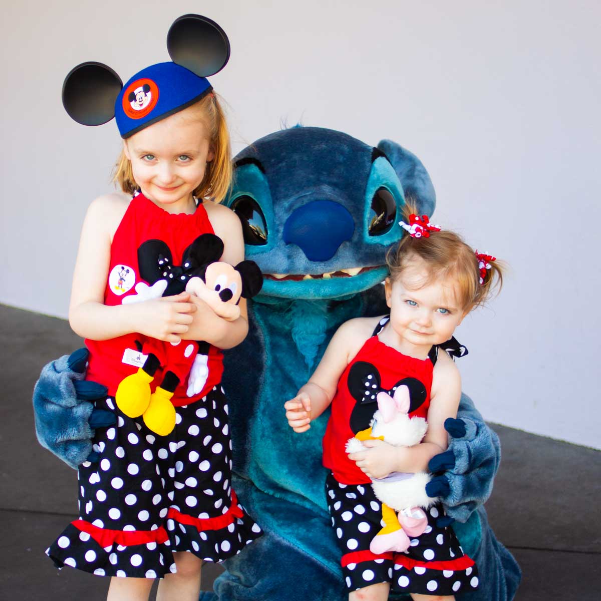Two young girls pose with Stitch at the Disney Parks.