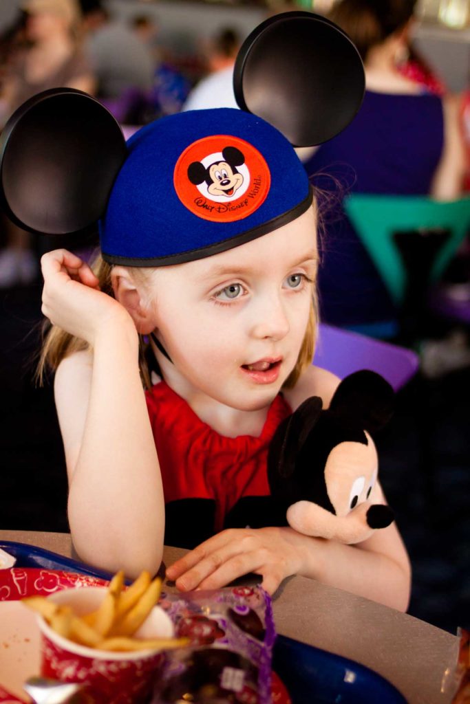 A young girl cuddles a stuffed Mickey Mouse toy and wears matching Mouse Ear hat.