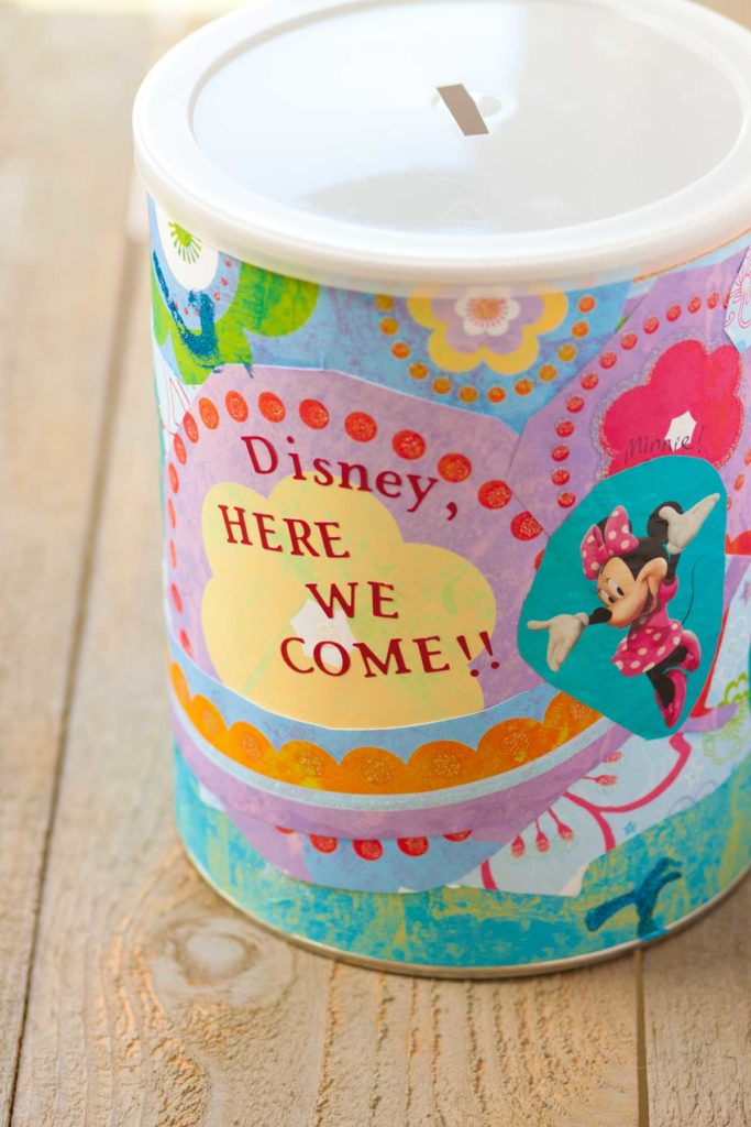 A cute tub has been decorated with papers to become a Disney savings jar.