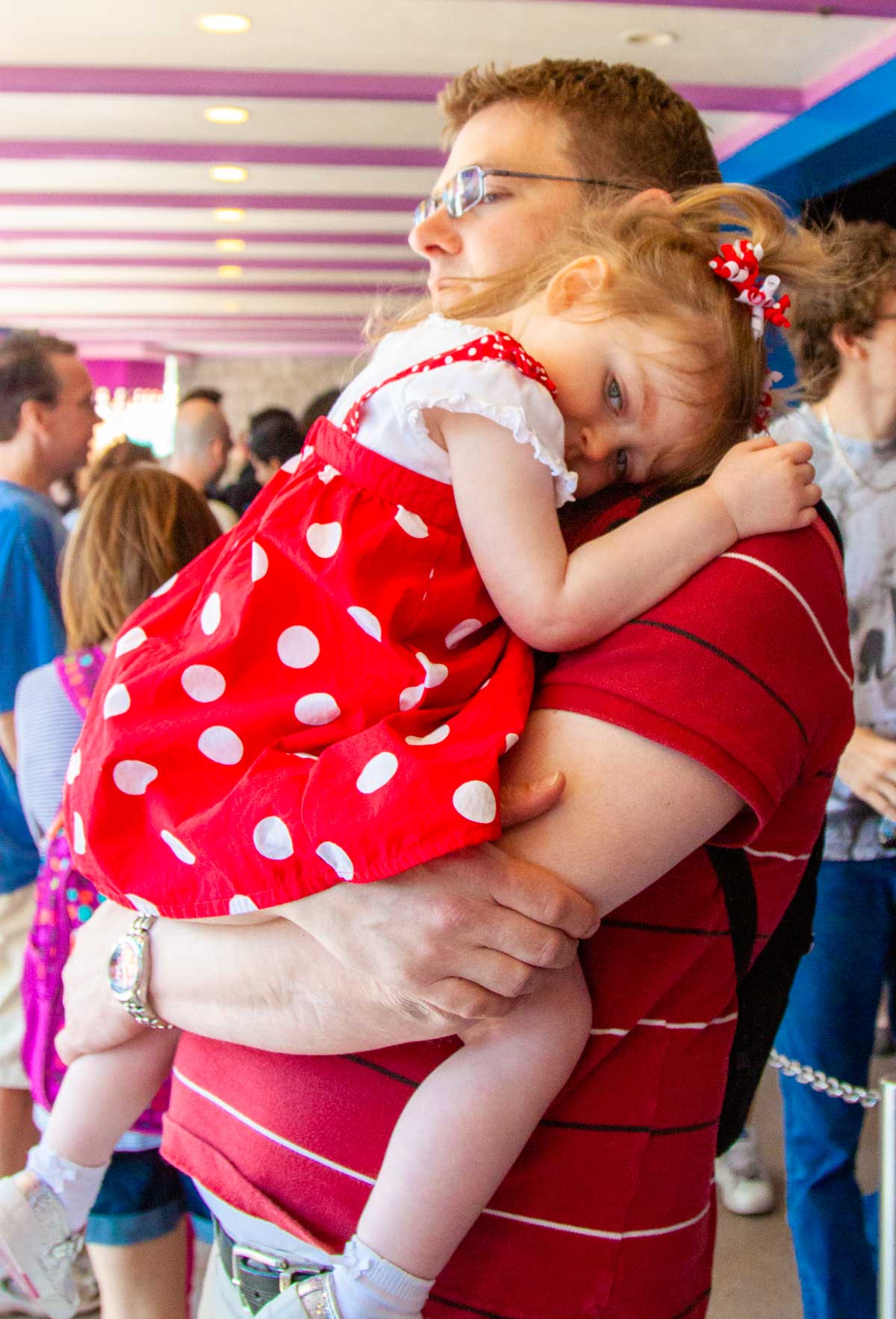 A dad holds his very tired toddler while waiting in line at Disney.