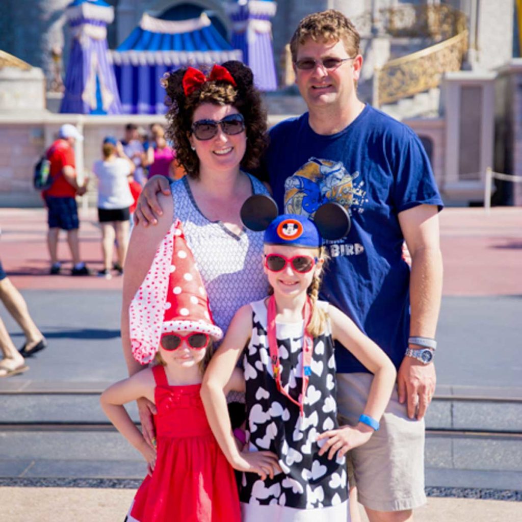 A family of four stands in front of the Disney castle in Florida.