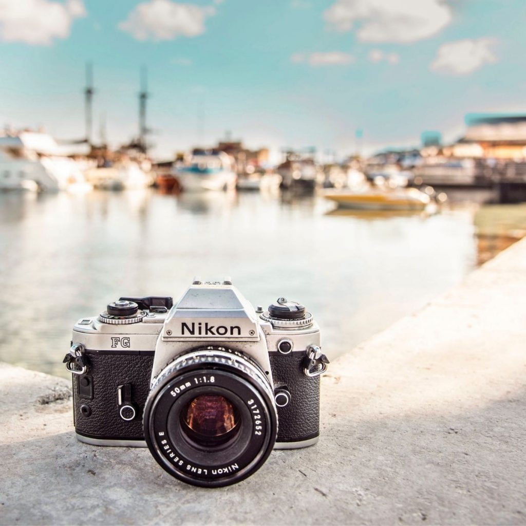 A DSLR camera sits on a ledge in front of water and a blue sky.