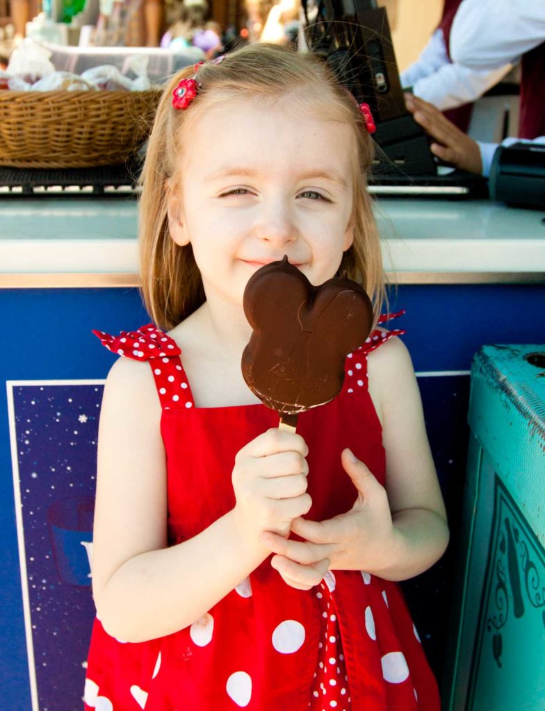 A young girl holds a chocolate coated Mickey ice cream treat at Disney World.