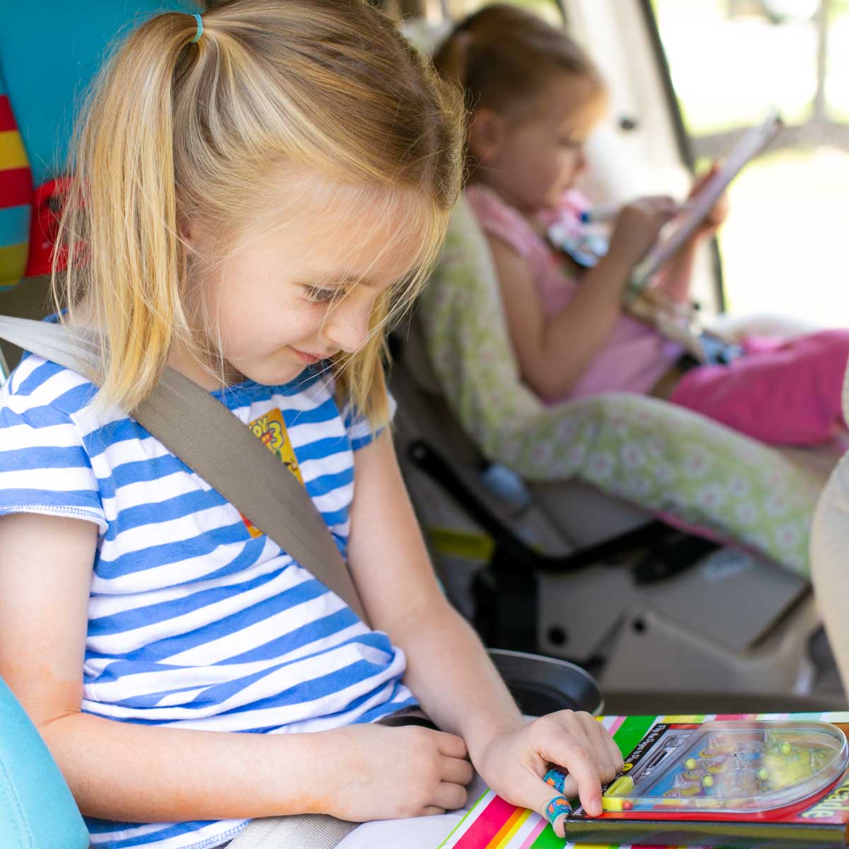 Two girls in the backseat of a car on a roadtrip.