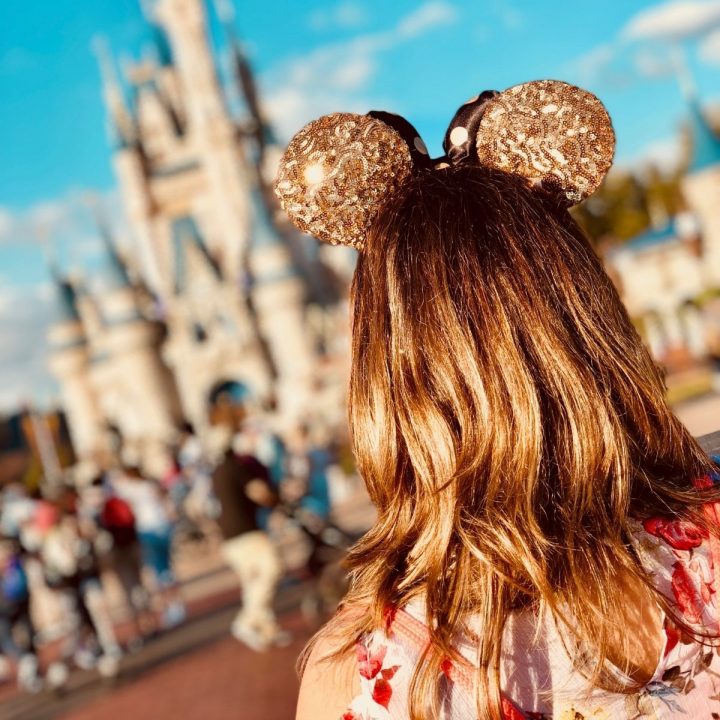 The back of a woman's head with mouse ears looking at the Disney castle.