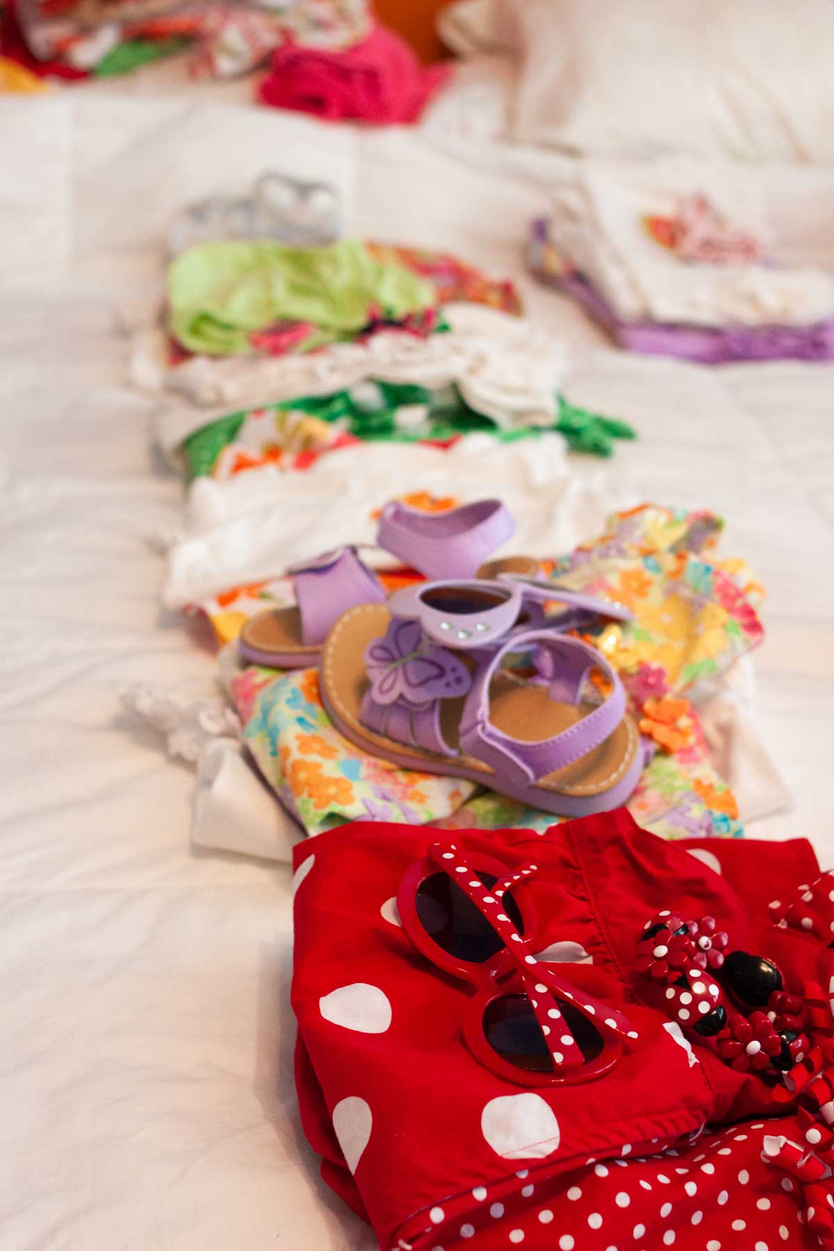 A pile of little girls' clothes and accessories are on a bed.