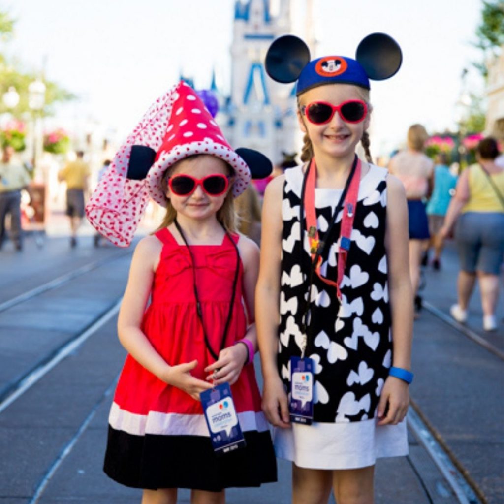 Adorable girls wearing red, black, and white outfits with Mouse Ear hats in front of the Disney Castle.