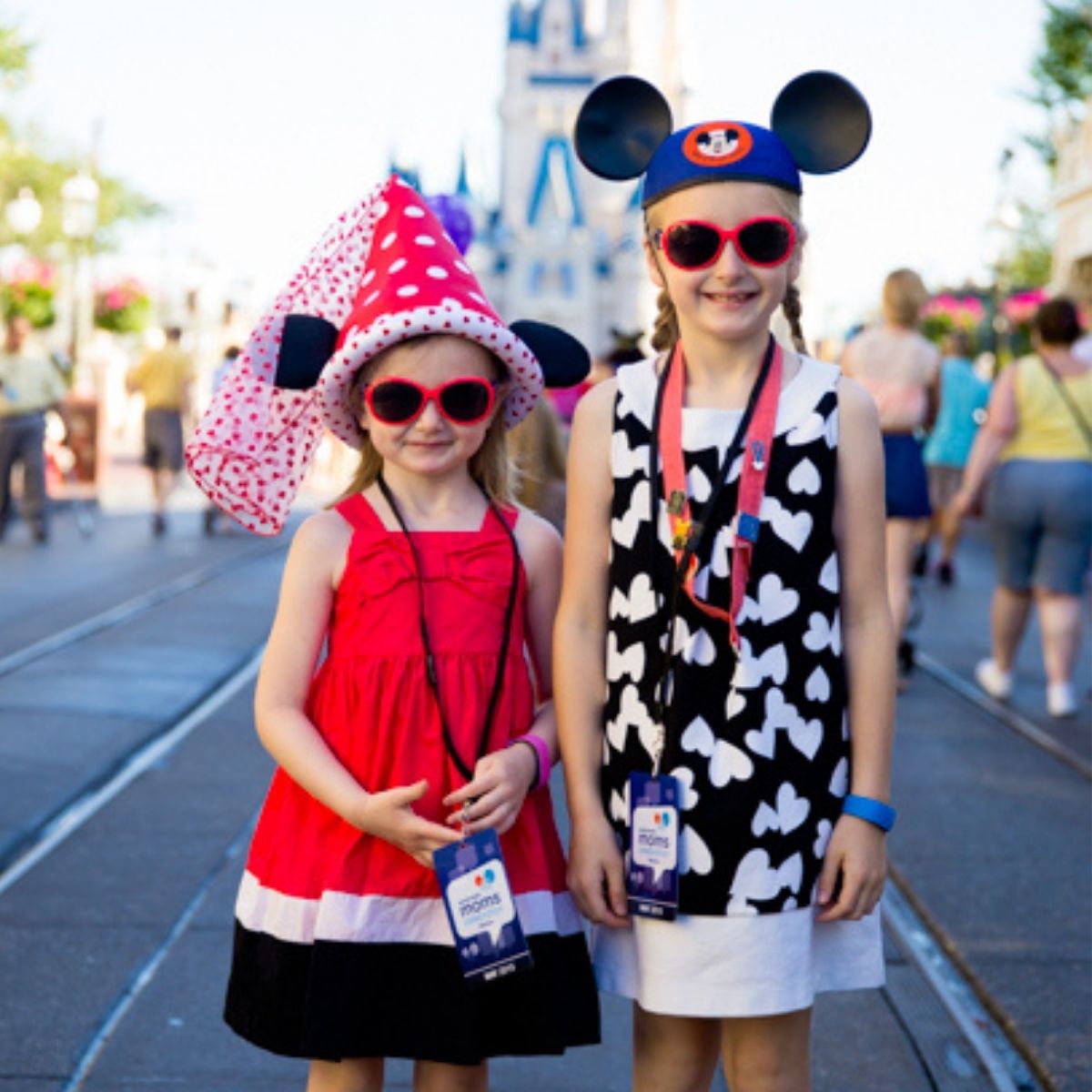 Adorable girls wearing red, black, and white outfits with Mouse Ear hats in front of the Disney Castle.