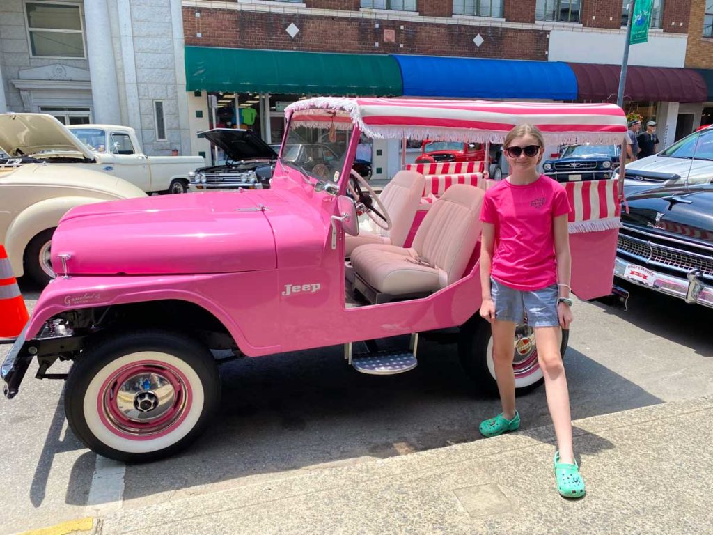 A girl stands in front of a pink jeep with pink and white striped canopy top.