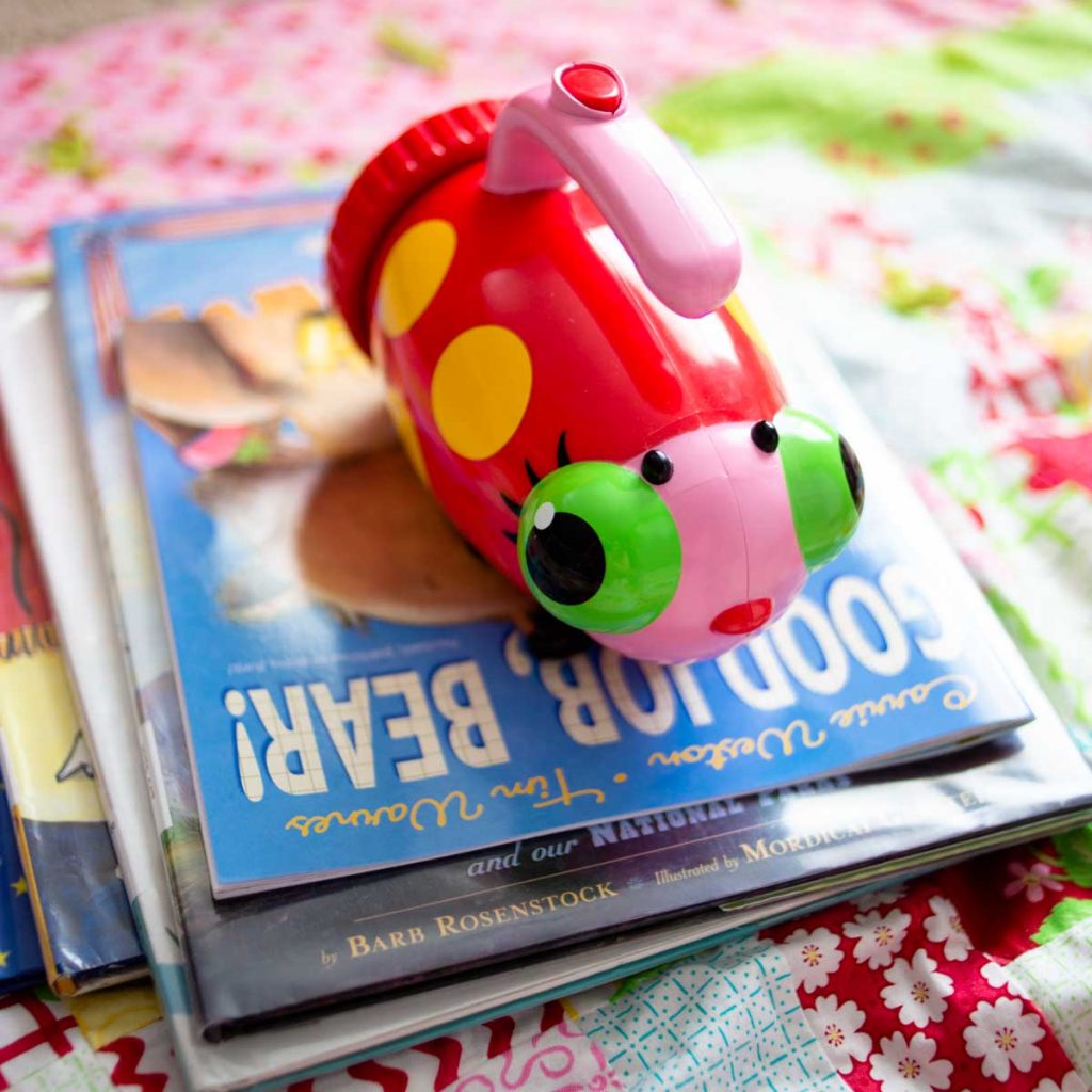 A pile of picture books about camping has a ladybug flashlight sitting on top.