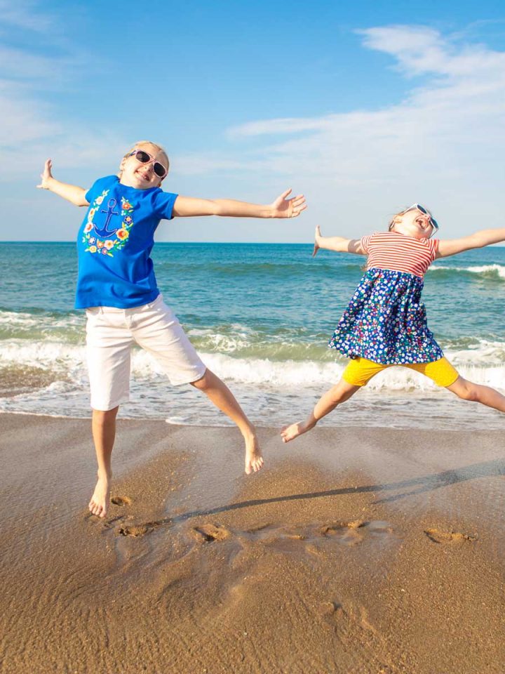 Two young girls are jumping for joy on the beach.