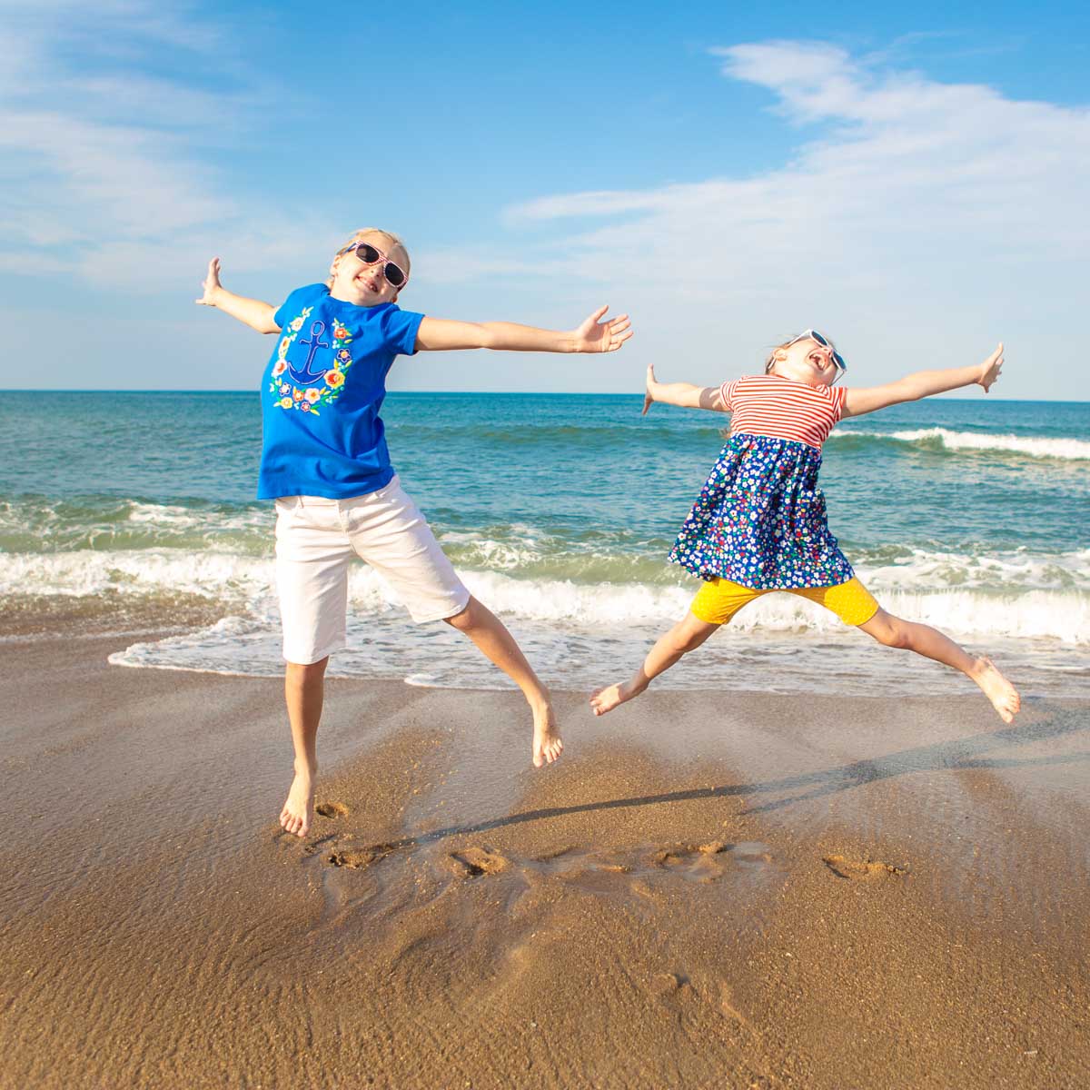 Two young girls are jumping for joy on the beach.