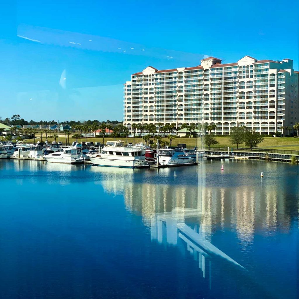 A high rise condo is on the water with boats floating in front.