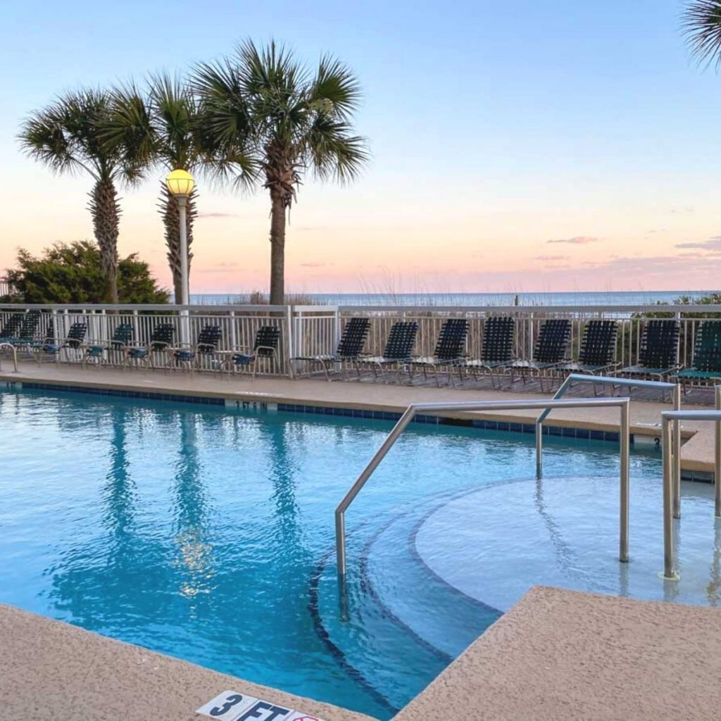 A pool with palm trees in the background at sunset.