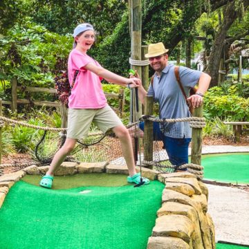 A young girl is mini golfing with her dad.
