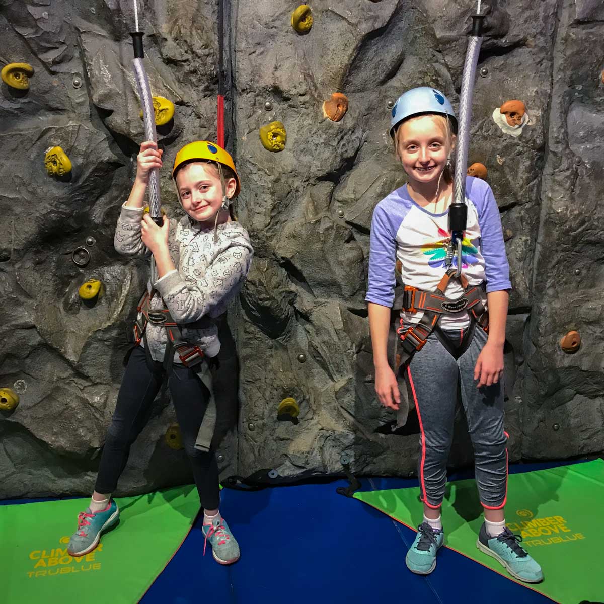 Two young girls are ready to rockwall climb with harnesses.