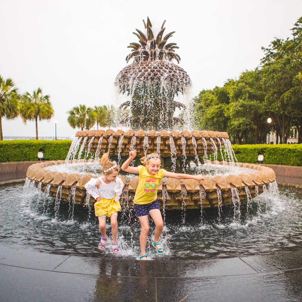 two young girls jump in the pineapple fountain in Charleston, SC.