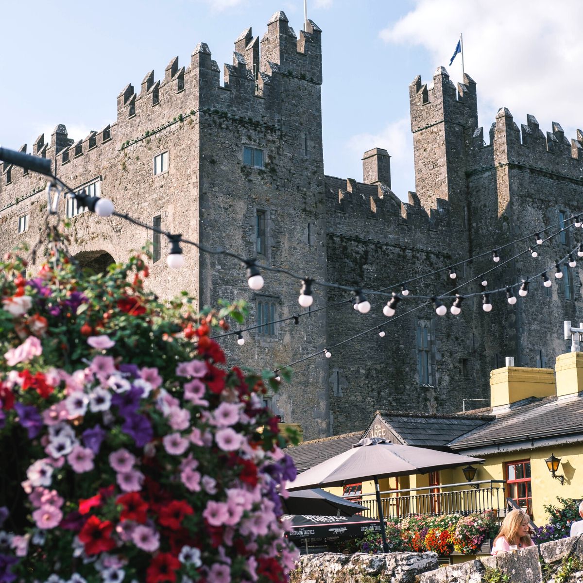 A castle in the background with bistro lights and fresh flowers at a cafe in front.