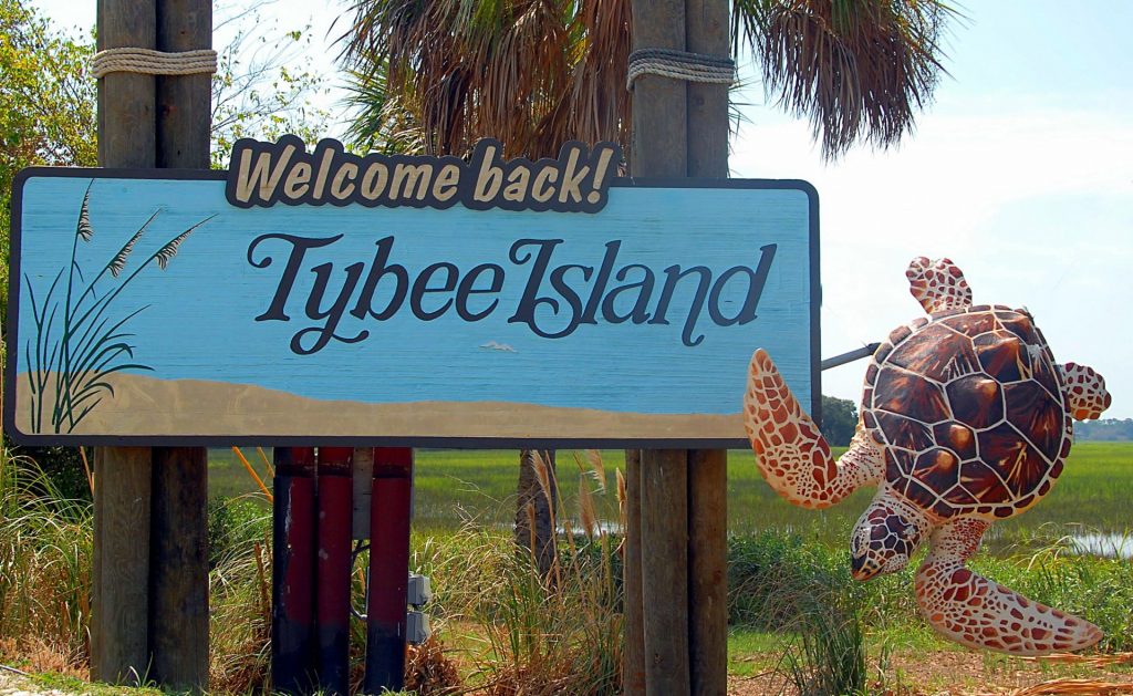 The blue painted sign says "Welcome Back! Tybee Island" and has a large 3D turtle on the side.