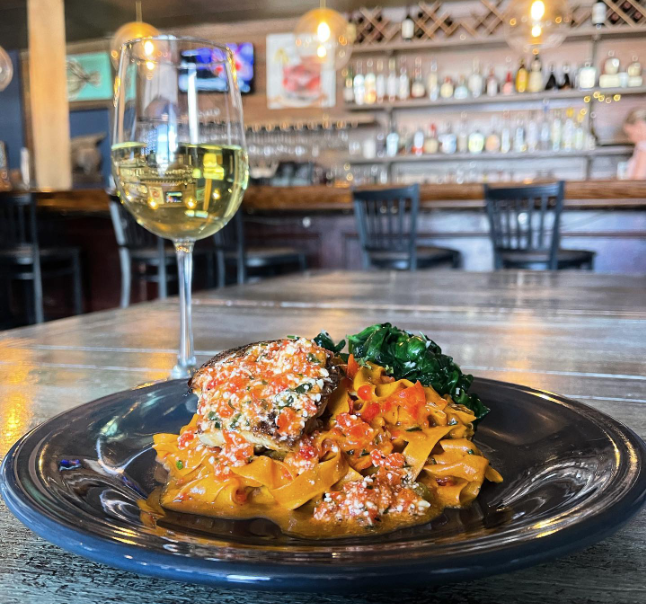 A plate of pasta next to a glass of wine on a table at the Sundae Cafe.