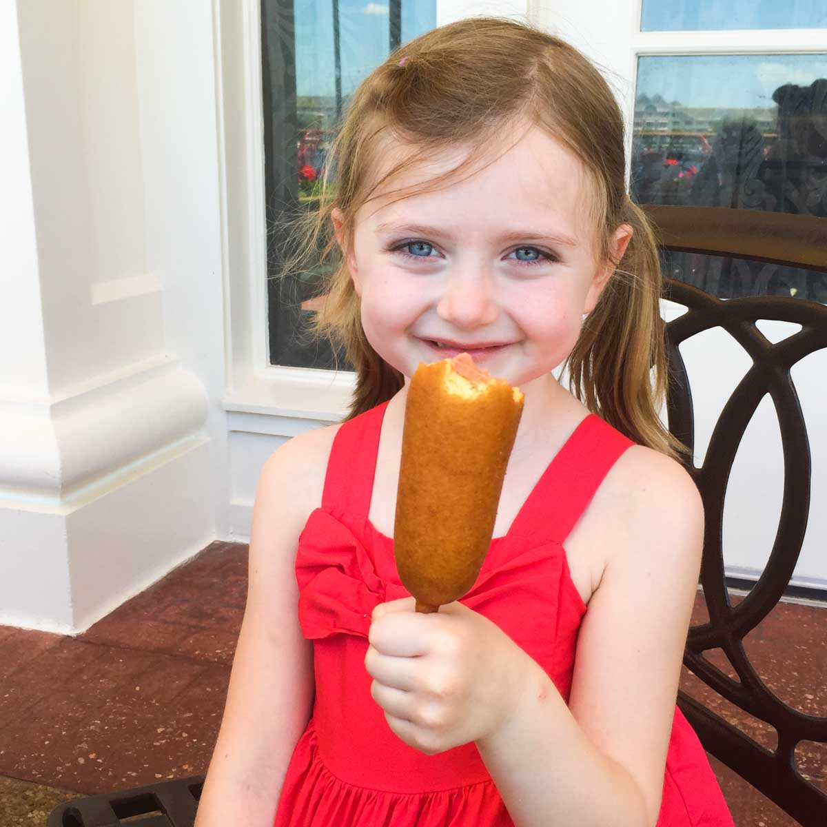 A young girl enjoys a corn dog in Magic Kingdom.